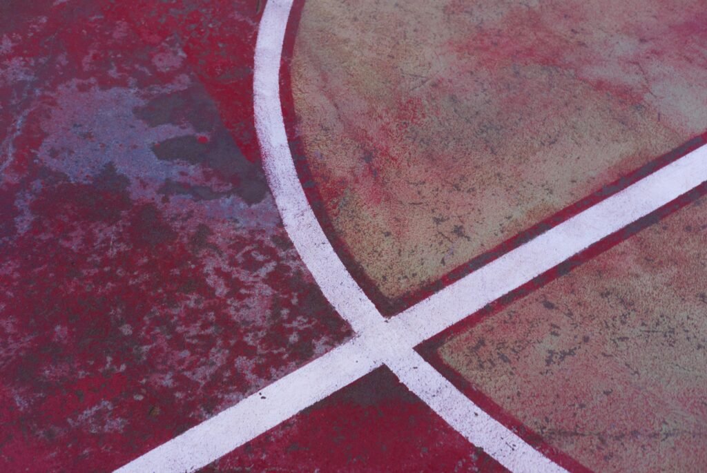 Nahaufnahme eines Basketballplatzes mit einem weißen Kreuz auf dem Boden, gut sichtbare Linien und strukturierter Asphalt