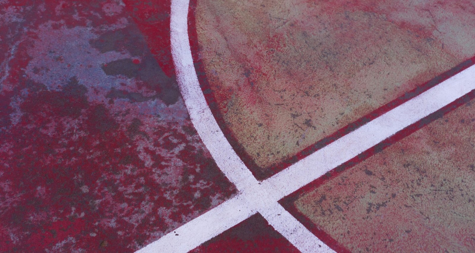 Nahaufnahme eines Basketballplatzes mit einem weißen Kreuz auf dem Boden, gut sichtbare Linien und strukturierter Asphalt