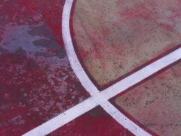 Nahaufnahme eines Basketballfelds, das eine weiße Kreuzmarkierung auf dem Boden zeigt, Fokus auf Linien und Asphaltstruktur