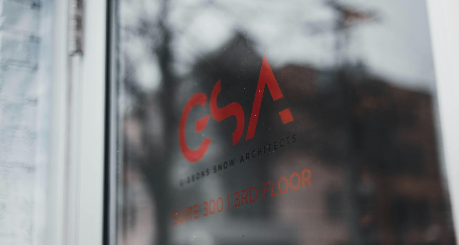 Nahaufnahme eines Fensterrahmens, im Hintergrund ist ein mehrstöckiges Gebäude erkennbar.