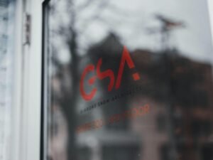 Nahaufnahme eines Fensters, im Hintergrund ist unscharf ein modernes Gebäude zu erkennen