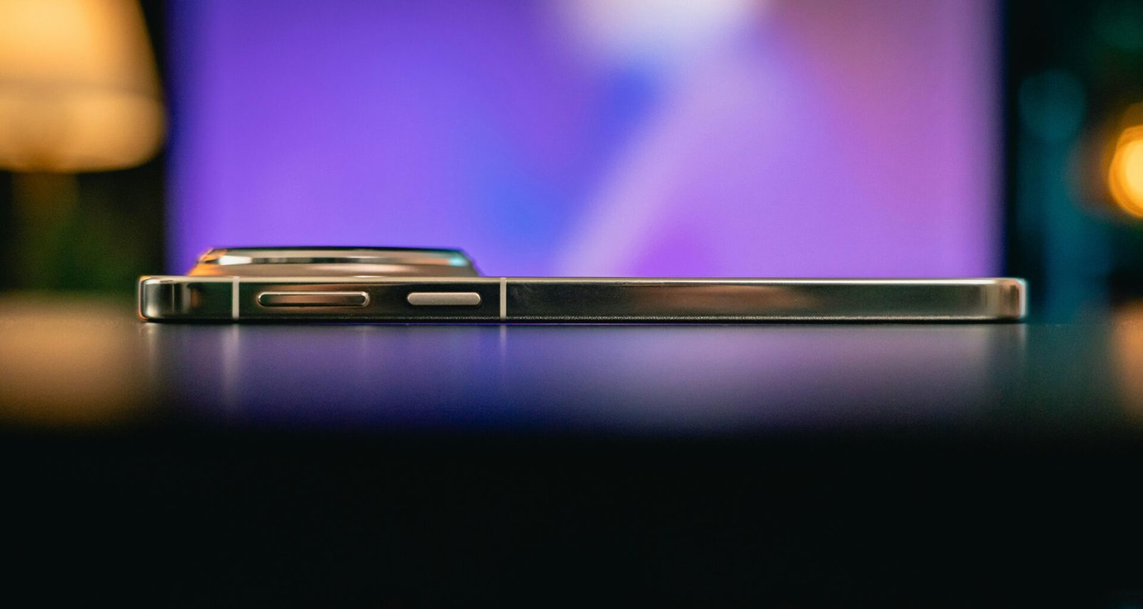 Seitliche Nahaufnahme eines Smartphones, das auf einer dunklen, glatten Oberfläche liegt.