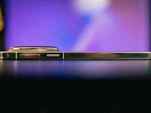 Seitliche Nahaufnahme eines Smartphones, das auf einer dunklen, glatten Oberfläche liegt.