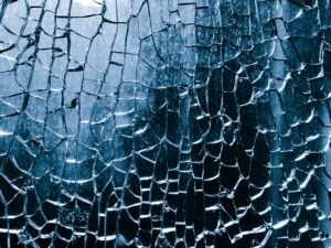 Nahaufnahme von zerbrochenem blauen Glas mit komplexen Rissen und Details in der Struktur.