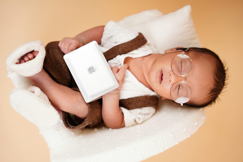 Schlafendes Neugeborenes mit runder Brille, Stirnband und Decke, aufgenommen in sanfter Beleuchtung