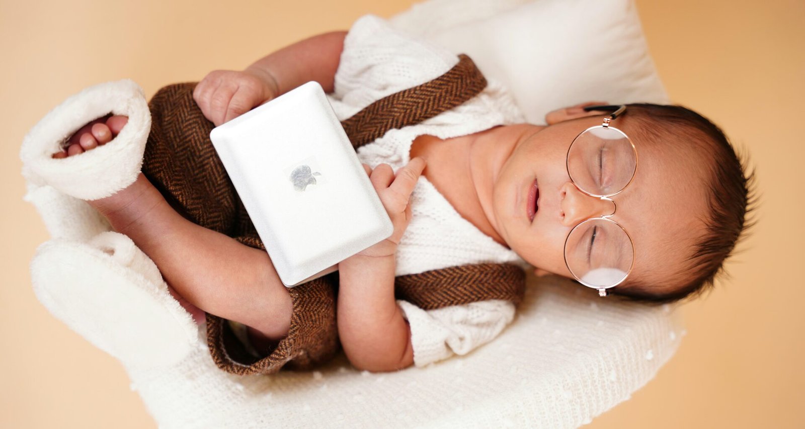 Schlafendes Neugeborenes mit runder Brille, Stirnband und Decke, aufgenommen in sanfter Beleuchtung