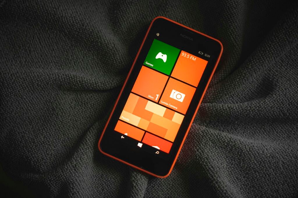 Orangefarbenes Smartphone mit bunten Kacheln auf dem Bildschirm, das auf einem neutralen Hintergrund liegt