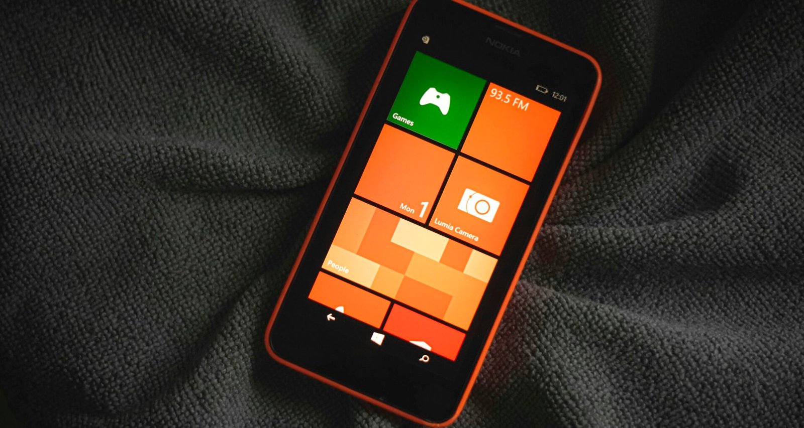 Orangefarbenes Smartphone mit bunten Kacheln auf dem Bildschirm, das auf einem neutralen Hintergrund liegt