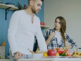 Ein Paar steht in einer Küche und streitet miteinander, umgeben von modernen Küchengeräten und hellem Licht.