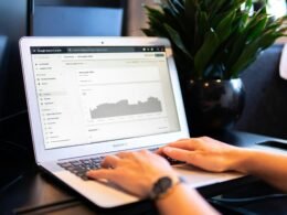 Person nutzt ein MacBook Air auf einem braunen Holztisch für den digitalen Arbeitsplatz im Homeoffice oder im Café.
