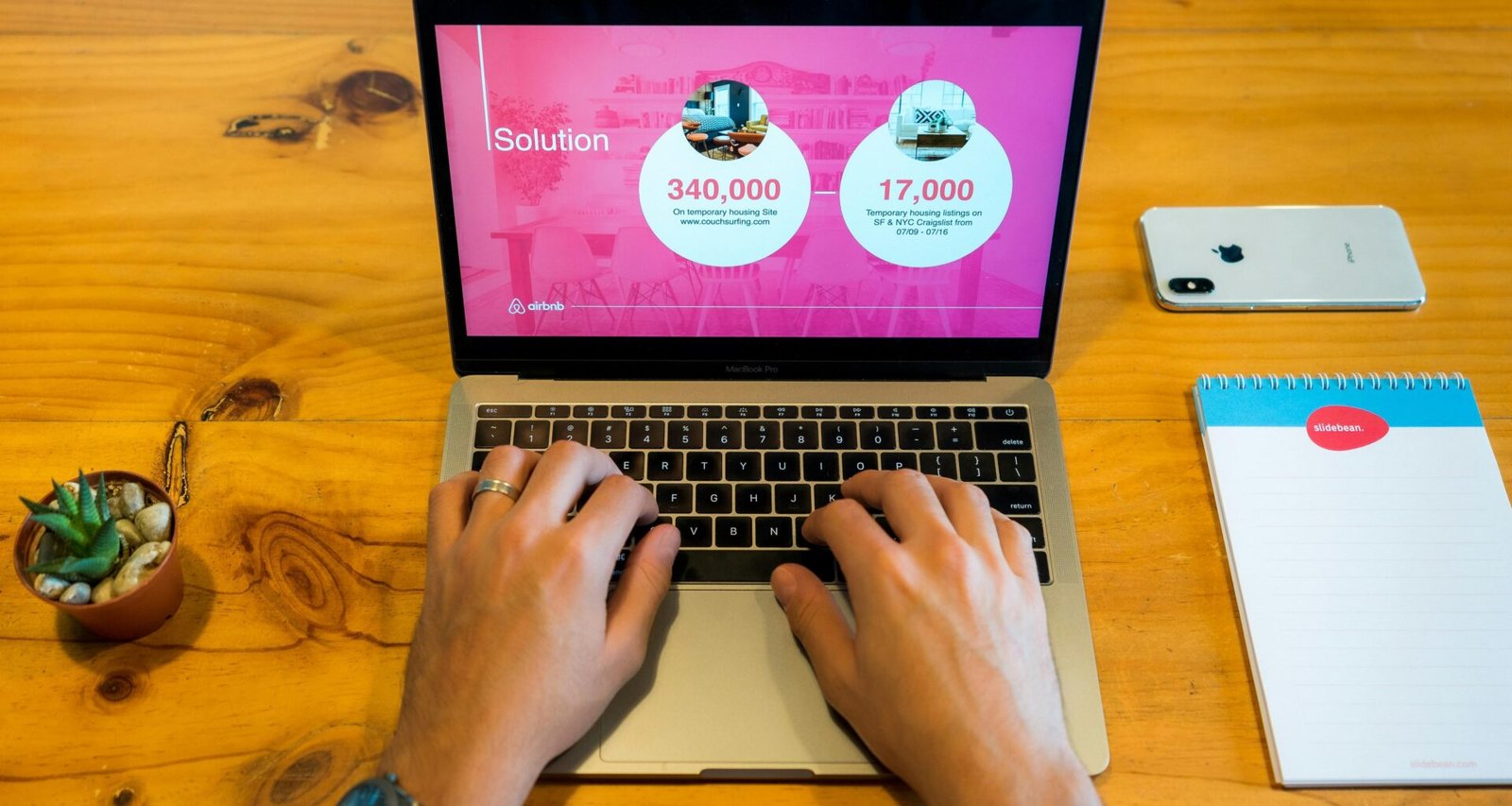 Person arbeitet mit einem MacBook Pro auf einem braunen Holztisch im modernen Arbeitsumfeld