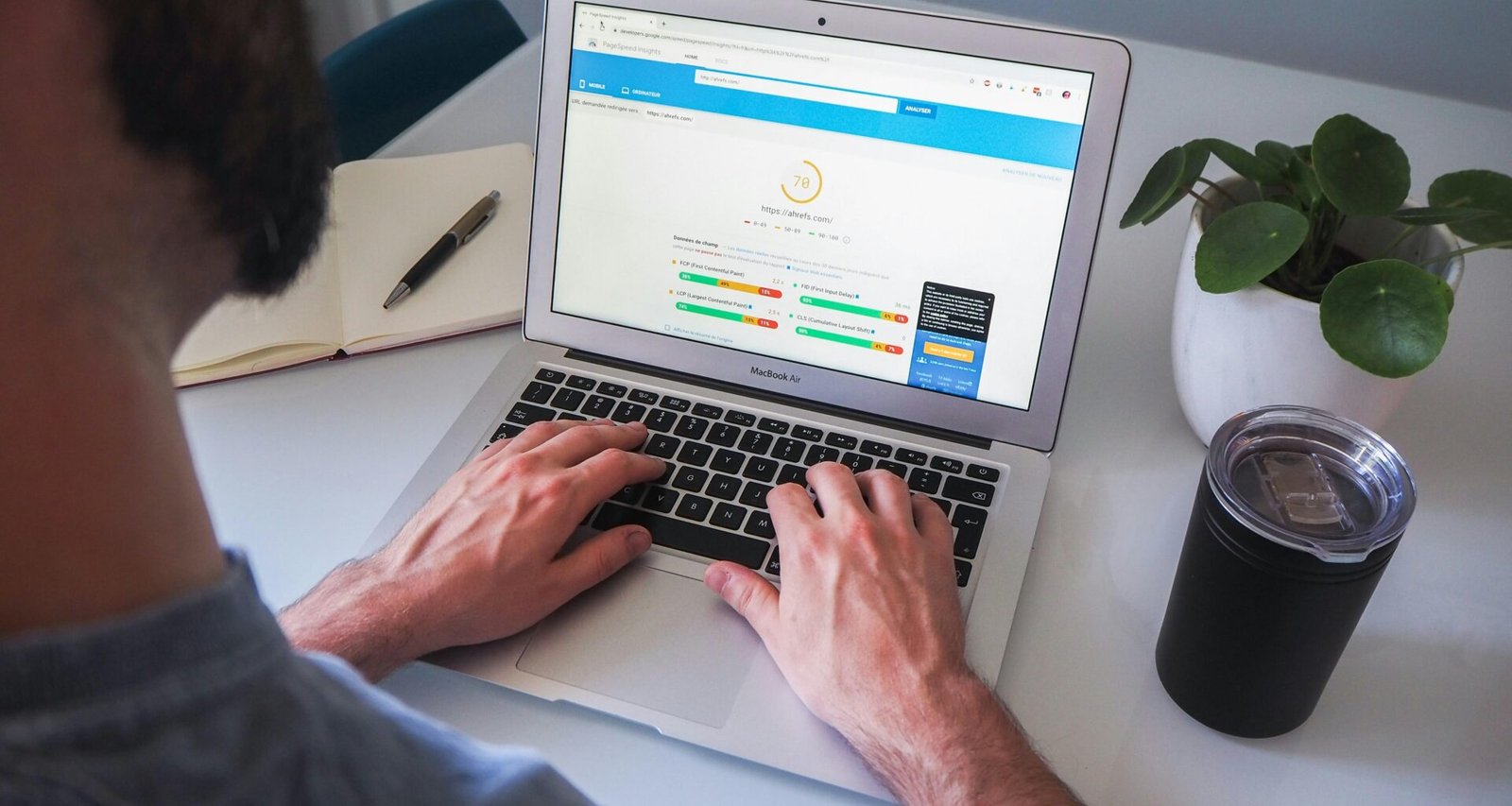 Person arbeitet an einem MacBook Pro auf einem weißen Tisch; ideale Arbeitsumgebung für digitales Arbeiten.