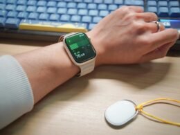 Person mit Smartwatch am Handgelenk tippt auf einem kleinen In-Ear-Monitor vor Tastaturhintergrund