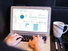 Person arbeitet an einem MacBook Pro auf einem schwarzen Tisch bei Tageslicht, ideal für Online-Marketing- oder Tech-Artikel