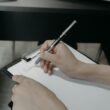 Person schreibt mit einem Kugelschreiber auf einem Clipboard und erstellt handschriftliche Notizen für die Arbeit.