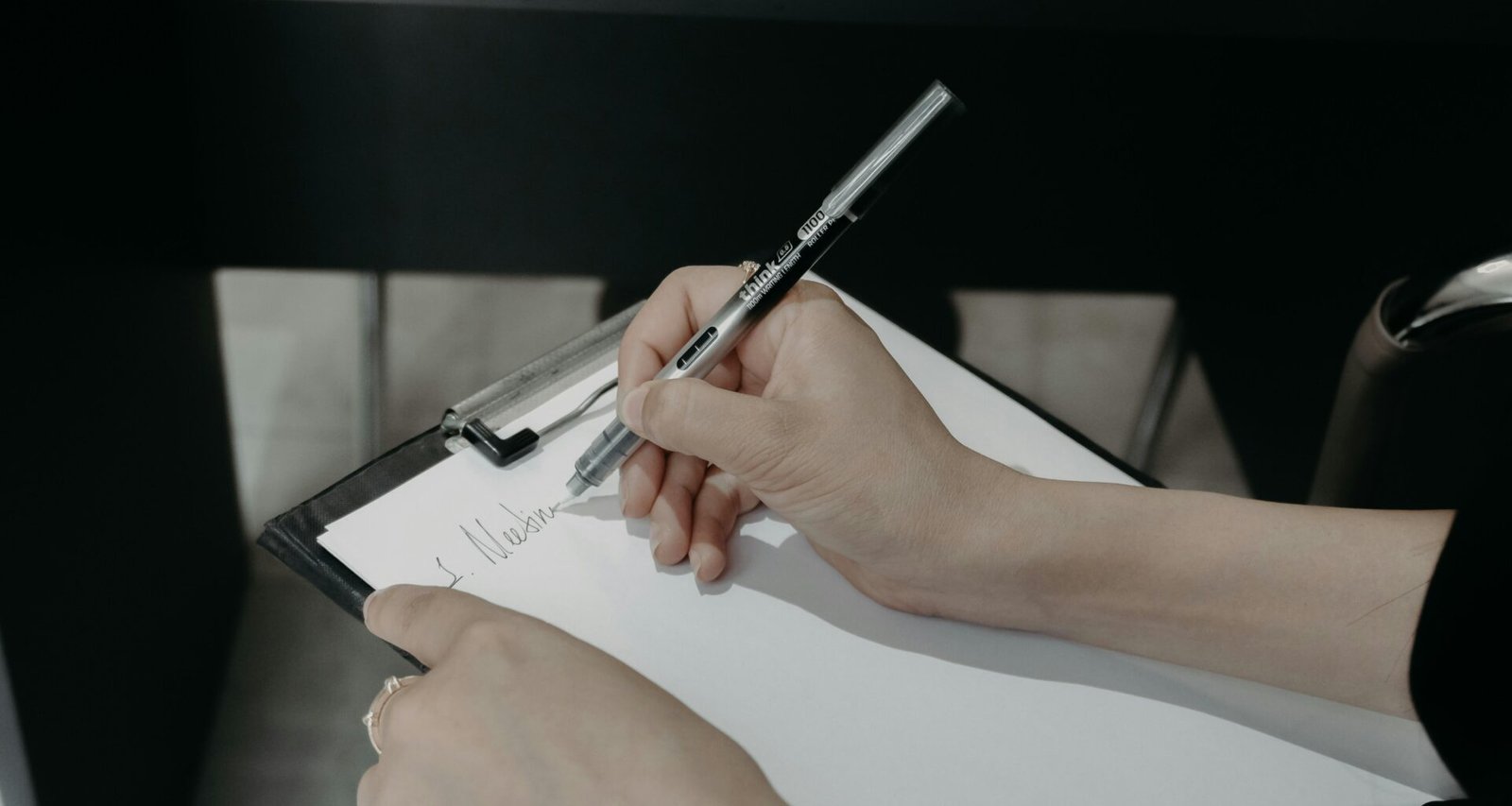 Person schreibt mit einem Kugelschreiber auf einem Clipboard und erstellt handschriftliche Notizen für die Arbeit.