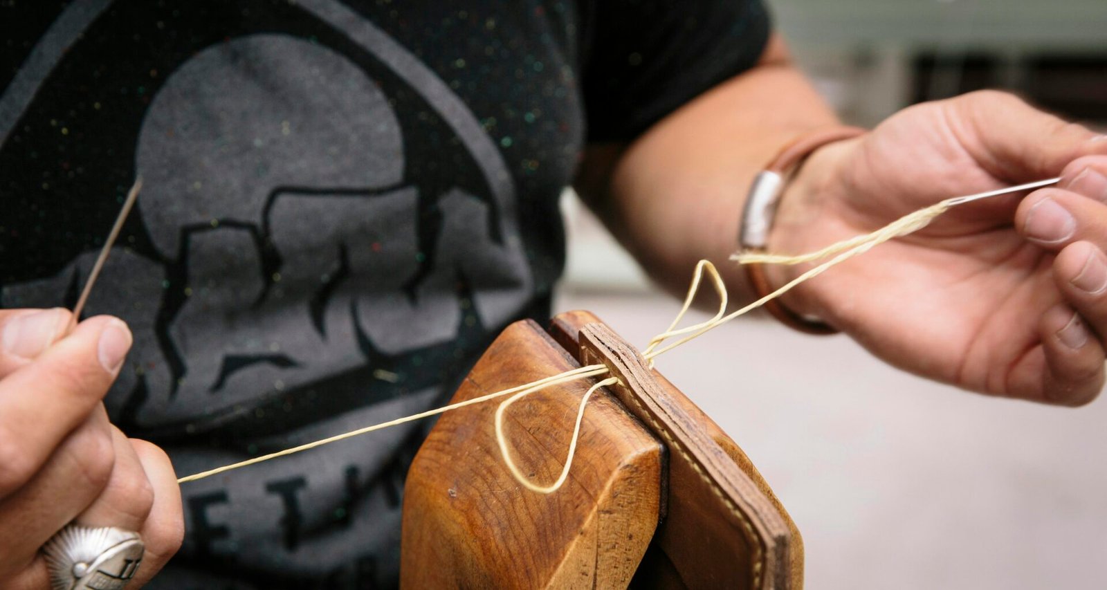 Person im schwarzen T-Shirt hält ein braunes Holz-Plektrum für die Gitarre in der Hand, Fokus auf das Plektrum