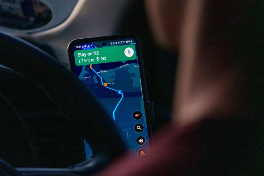 Eine Person sitzt im Auto und nutzt eine Navigations-App auf dem Smartphone zur Routenplanung während der Fahrt.