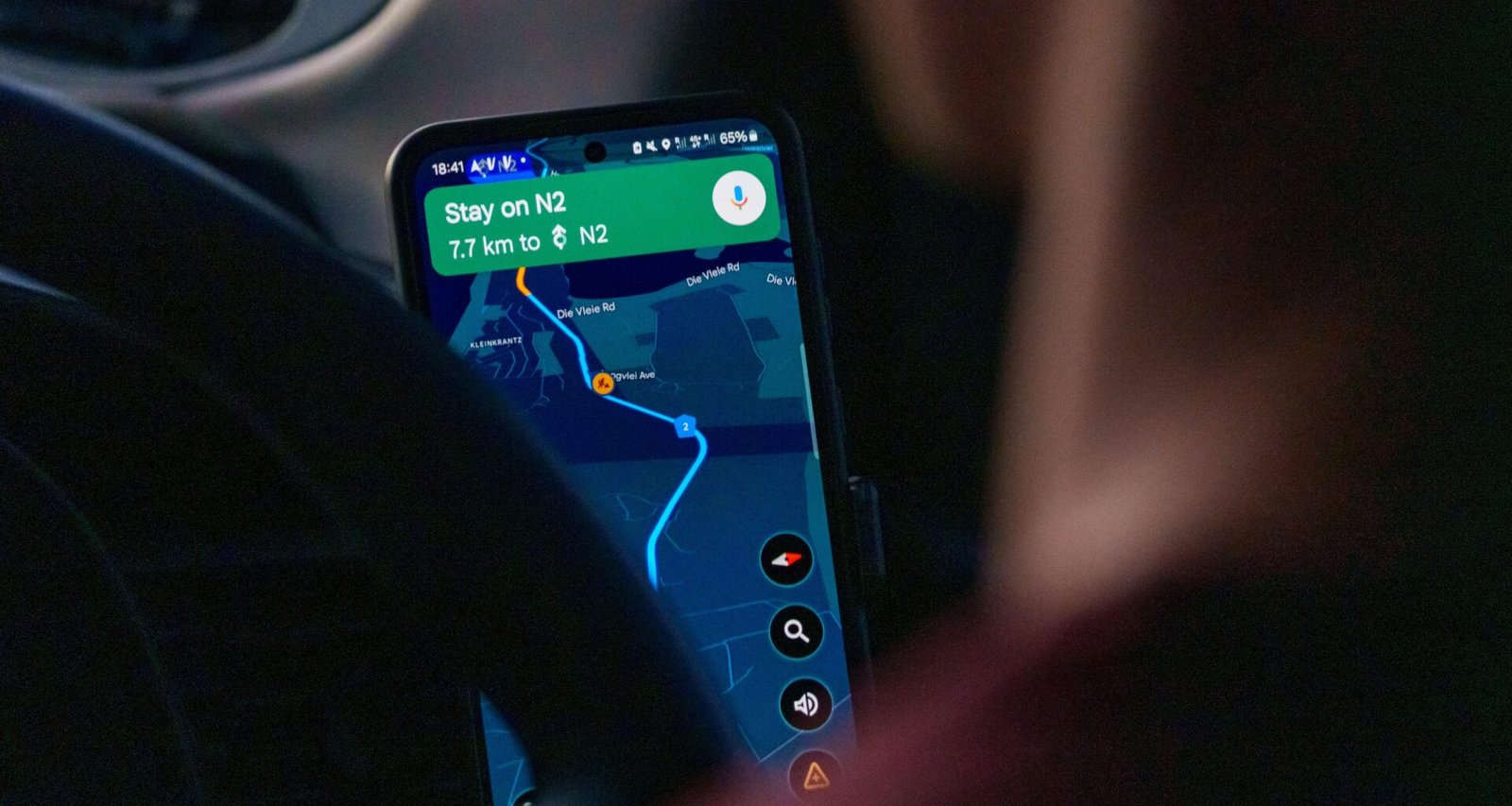 Eine Person sitzt im Auto und nutzt eine Navigations-App auf dem Smartphone zur Routenplanung während der Fahrt.