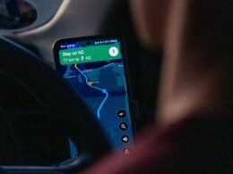 Eine Person sitzt im Auto und nutzt eine Navigations-App auf dem Smartphone zur Routenplanung während der Fahrt.