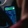 Person navigiert mit einer App auf dem Smartphone am Steuer eines Autos, Blick auf Bildschirm und Armaturen