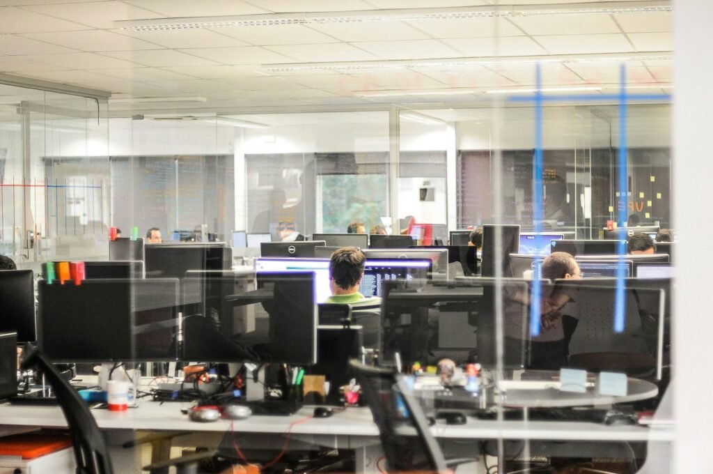 Mehrere Personen nutzen Desktop-Computer in einem modernen Büroraum und arbeiten an verschiedenen Aufgaben im Team.