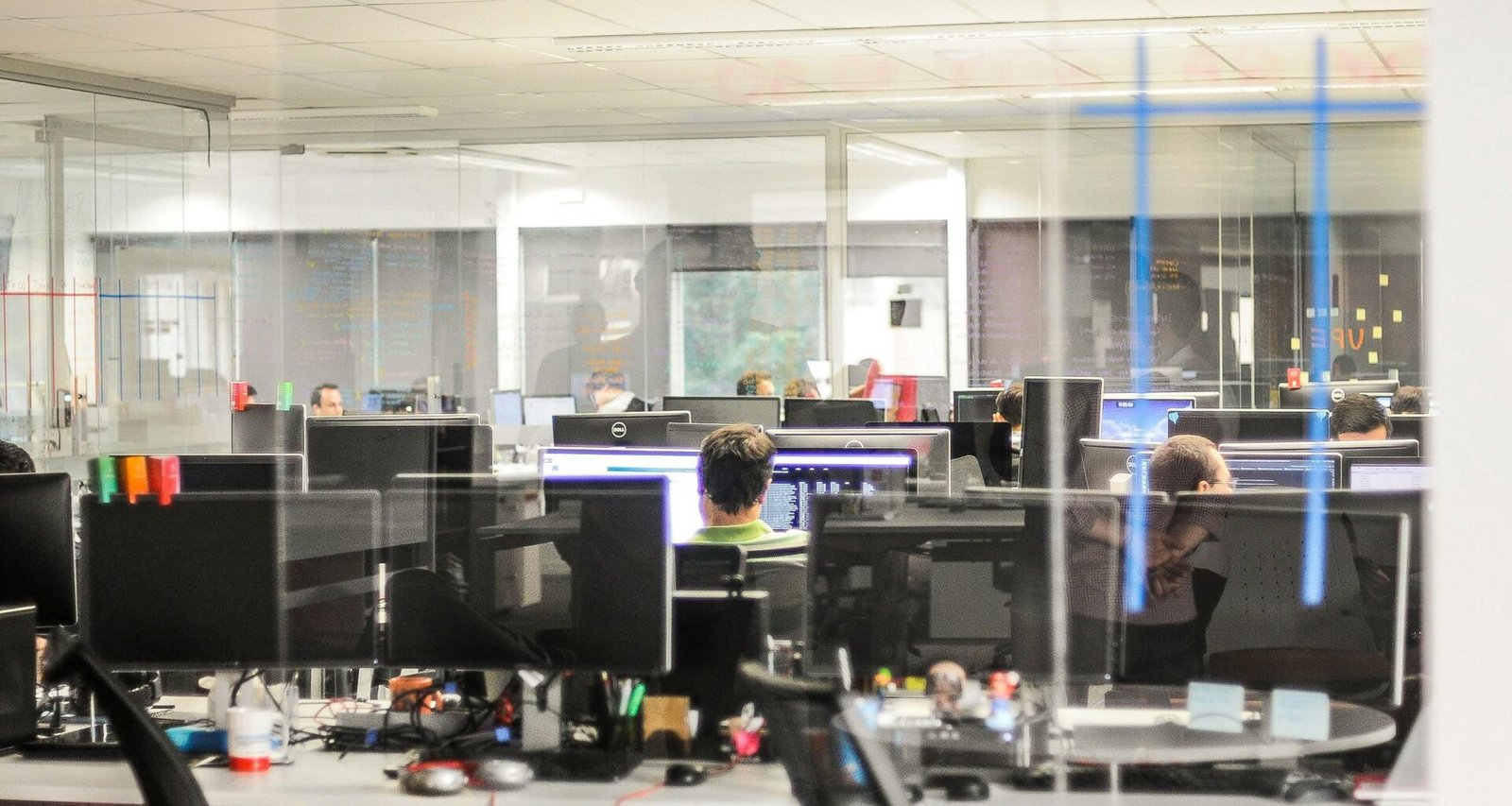 Mehrere Personen nutzen Desktop-Computer in einem modernen Büroraum und arbeiten an verschiedenen Aufgaben im Team.
