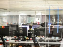 Mehrere Personen nutzen Desktop-Computer in einem modernen Büroraum und arbeiten an verschiedenen Aufgaben im Team.