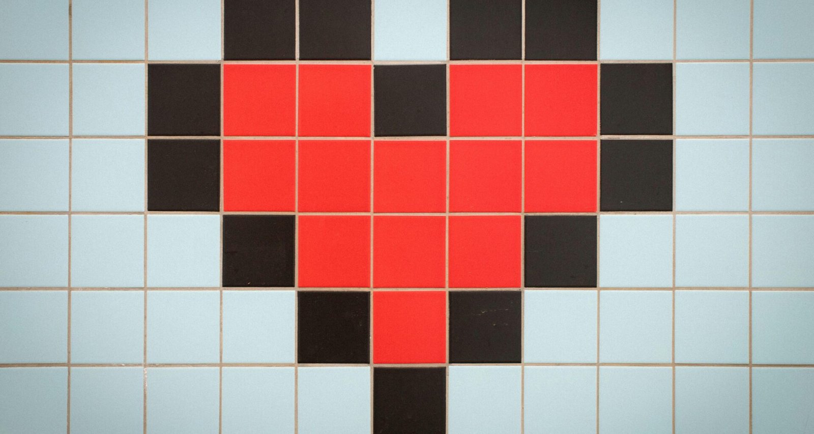 Rotes pixeliertes Herz auf hellem, blau gekacheltem Hintergrund als Symbol für digitale Themen und Webtechnologien