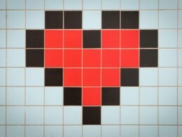 Rotes pixeliertes Herz auf hellem, blau gekacheltem Hintergrund als Symbol für digitale Themen und Webtechnologien