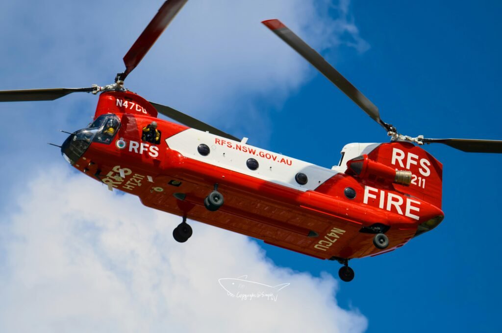 Rot-weißer Feuerwehrhubschrauber bei Tageslicht im Flug vor wolkenlosem, blauem Himmel