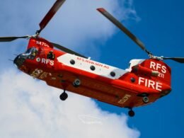 Rot-weißer Feuerwehrhubschrauber bei Tageslicht im Flug vor wolkenlosem, blauem Himmel