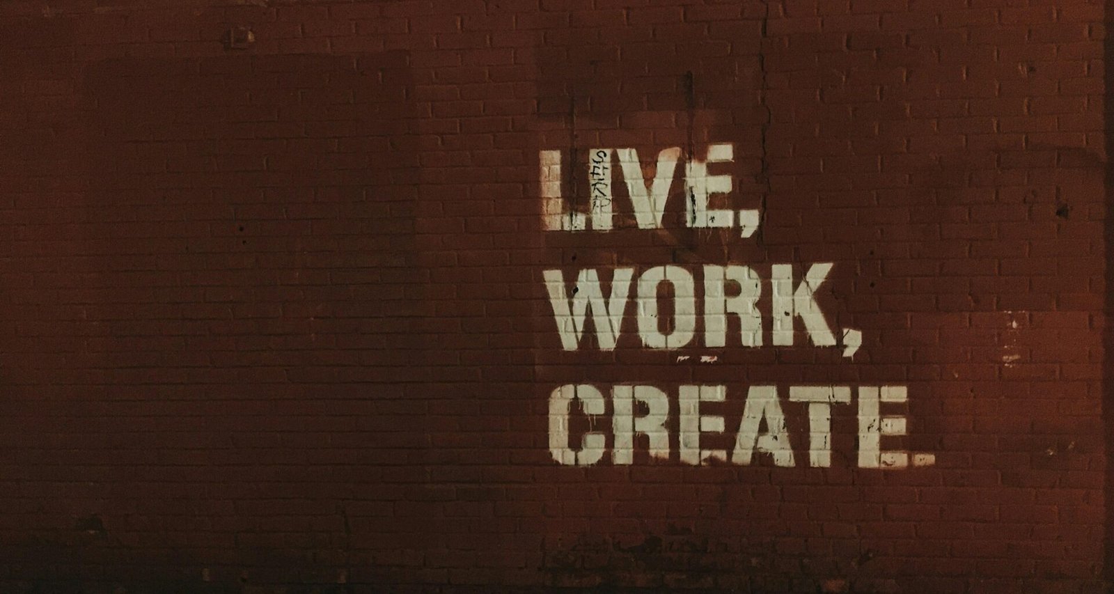 Rote Backsteinwand mit weißem Graffiti-Zitat live, work, create. als Inspiration für Arbeits- und Kreativräume.