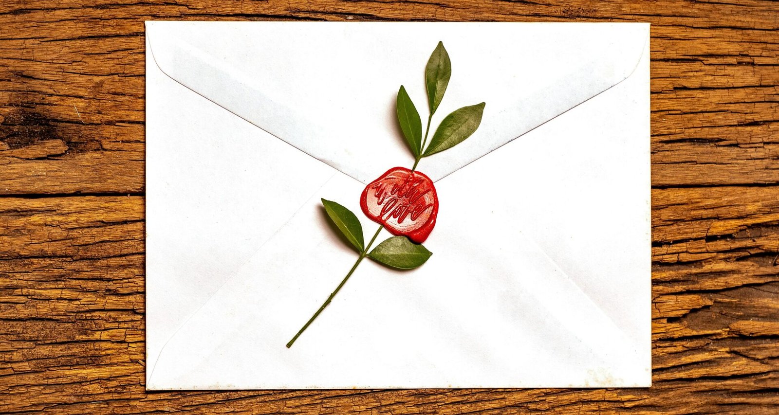 Rote Rose liegt auf verschlossenem weißen Briefumschlag als zentrales Element im Fotomotiv.
