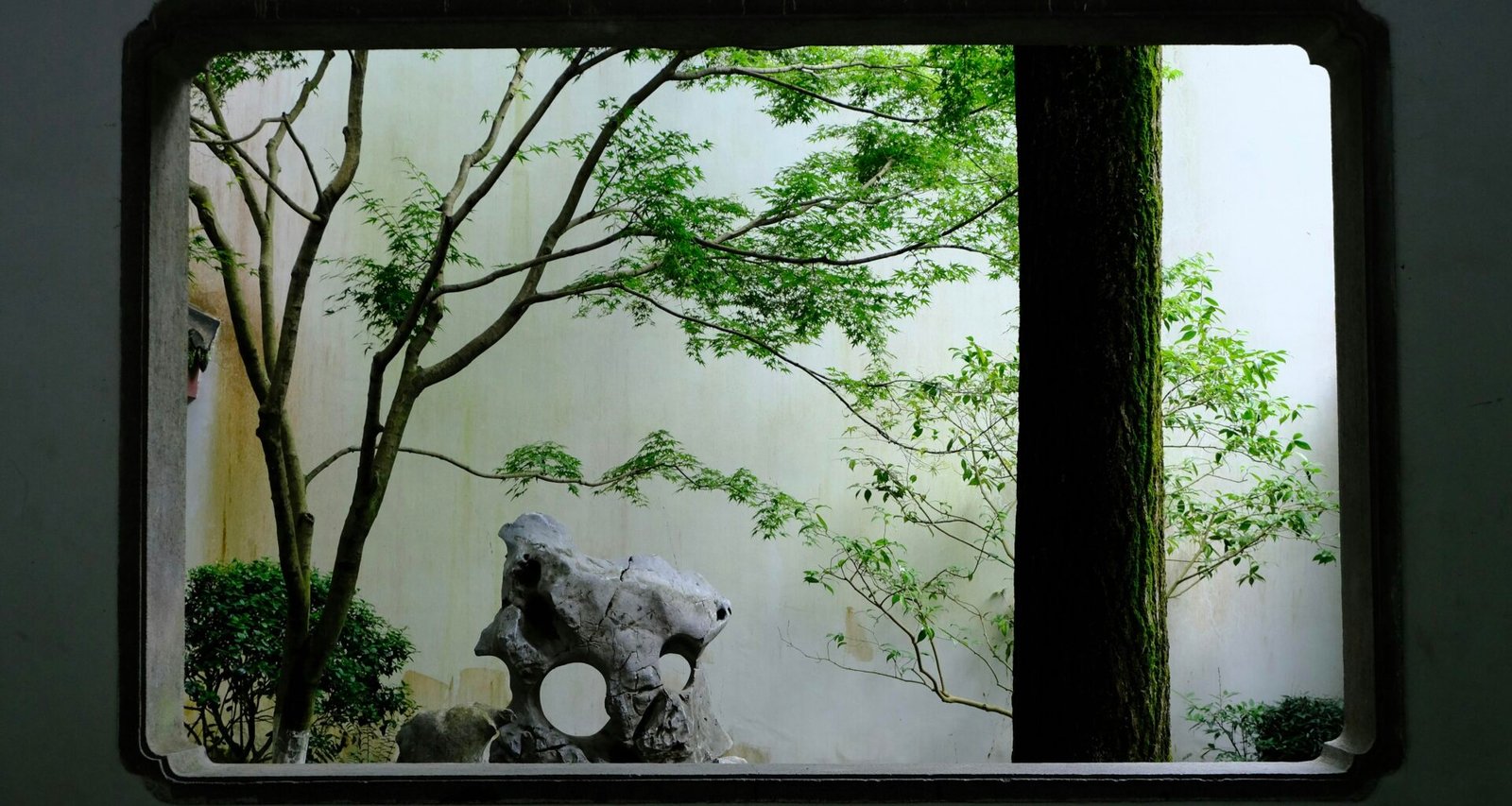 Ein dekoratives Fenster eröffnet den Blick auf einen friedlichen Garten mit grüner Vegetation im Hintergrund.