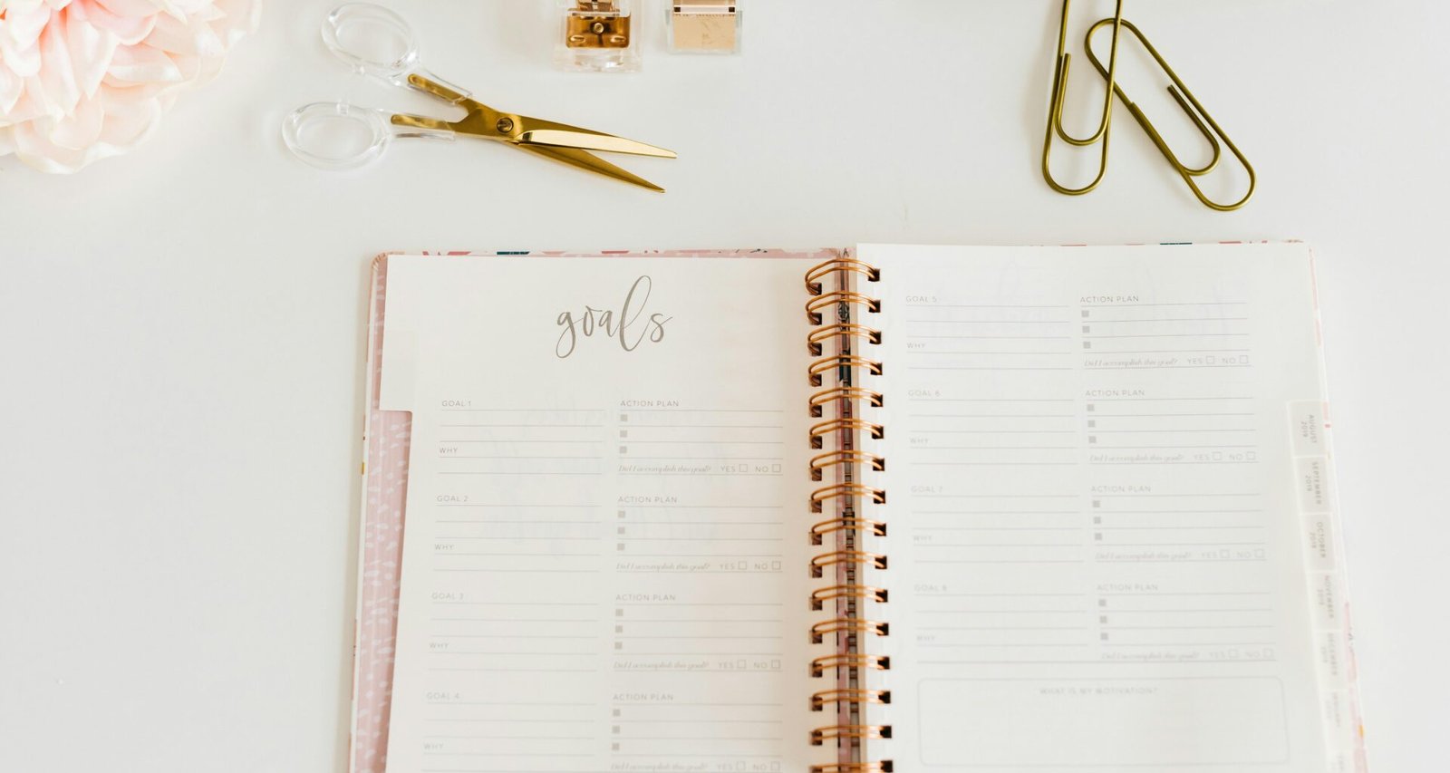 Offenes Spiralnotizbuch, daneben eine Schere und zwei Büroklammern auf einem weißen Tisch. Bürobedarf zur Organisation.