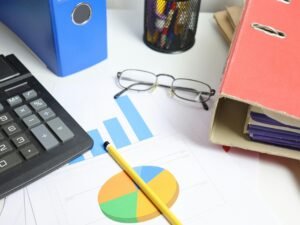 Schreibtisch mit Taschenrechner, ausgedruckten Diagrammen und mehreren Ordnern, geeignet für Themen rund um Büroarbeit und Finanzen.