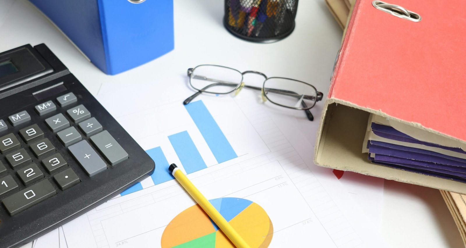 Schreibtisch mit Taschenrechner, Diagrammen und Ordnern – Darstellung von Arbeitsorganisation und analytischer Planung