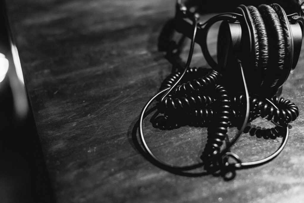 Schwarze und weiße Kopfhörer mit Spiralkabel liegen mittig auf einem Tisch, fotografiert aus der Vogelperspektive.