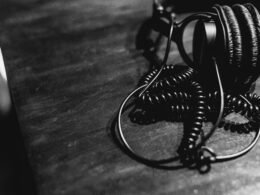 Schwarze und weiße Kopfhörer mit Spiralkabel liegen mittig auf einem Tisch, fotografiert aus der Vogelperspektive.