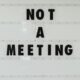 Schwarzes Schild mit der Aufschrift 'Note a meeting' an einer weißen Wand in einem modernen Bürogebäude.