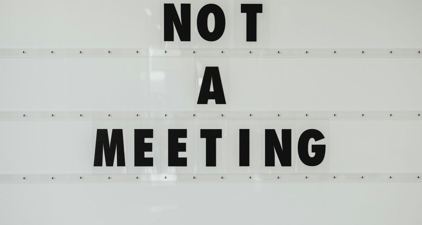 Schwarzes Notizschild mit Meeting-Aufschrift an weißer Wand als Orientierung für Büro- oder Arbeitsräume