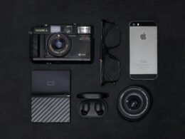 Ein silbernes iPhone 6 liegt neben einer schwarzen und grauen Kamera auf einer ebenen Fläche.
