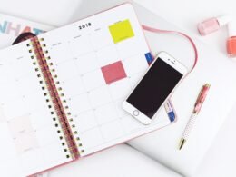 Silberfarbenes iPhone 6 auf weißem Spiral-Notizbuch, flach fotografiert, geeignet für Themen rund um Technik und Produktivität.