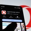 Ein Smartphone-Bildschirm mit geöffneter Opera Browser-App und sichtbaren KI-Funktionen auf einem Holztisch