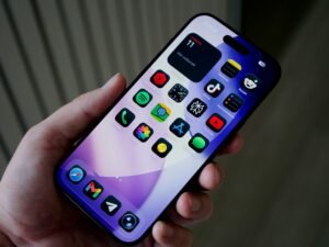 Hand hält ein Smartphone mit einer Vielzahl farbiger App-Icons auf dem Bildschirm vor unscharfem Hintergrund