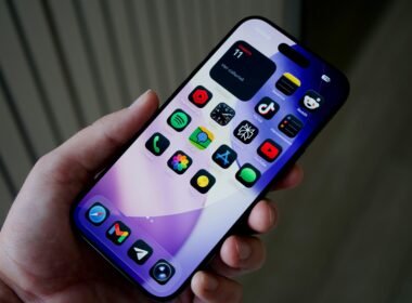 Hand hält ein Smartphone mit einer Vielzahl farbiger App-Icons auf dem Bildschirm vor unscharfem Hintergrund