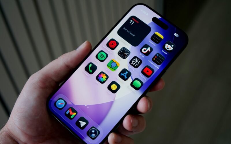 Hand hält ein Smartphone mit einer Vielzahl farbiger App-Icons auf dem Bildschirm vor unscharfem Hintergrund
