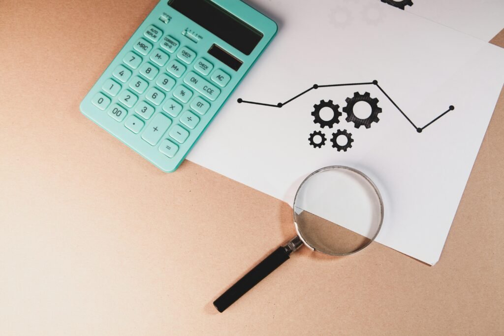 Ein Taschenrechner, eine Lupe und ein Papier mit Diagramm und Zahnrädern zeigen Analyse- und Optimierungsprozesse im Online-Marketing.
