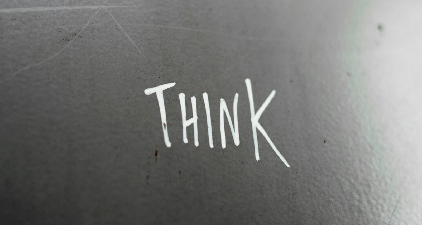 Weiße Wand mit großem schwarzen Schriftzug 'think', aufgenommen von Rob Coates. Klare Linien und minimalistisches Design.